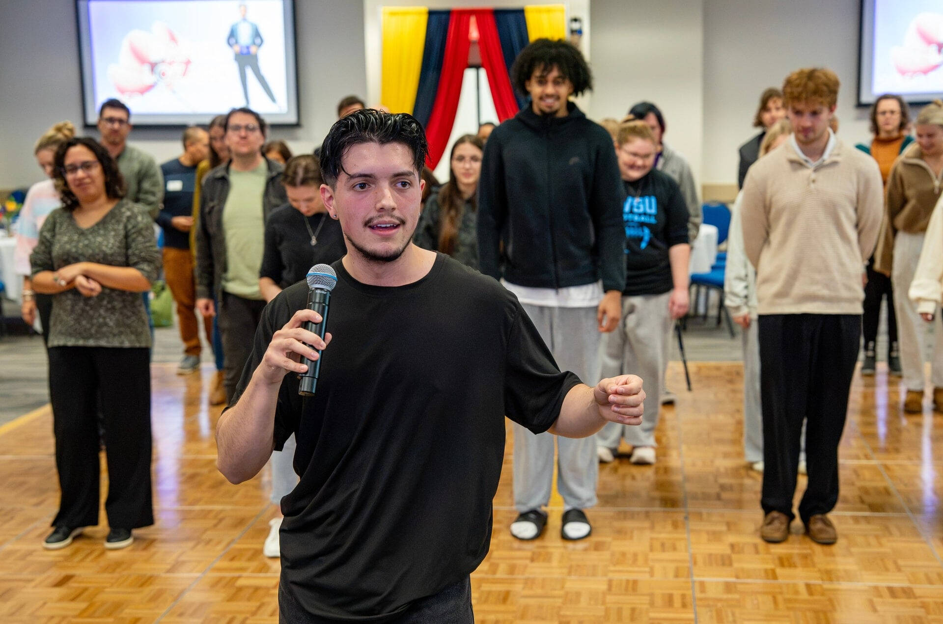 Daniel Lozano, with microphone, leads a dance class of people standing on a dance floor